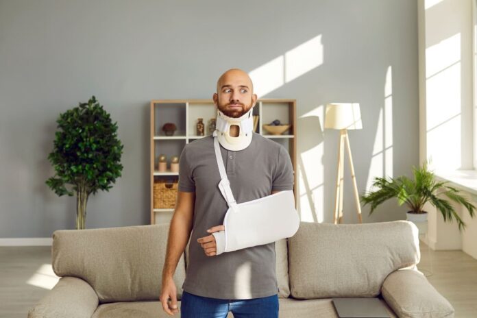 Kaskokindlustuse liisingmaksekindlustus - kaelatoe ja kipsis käega mees keset tuba