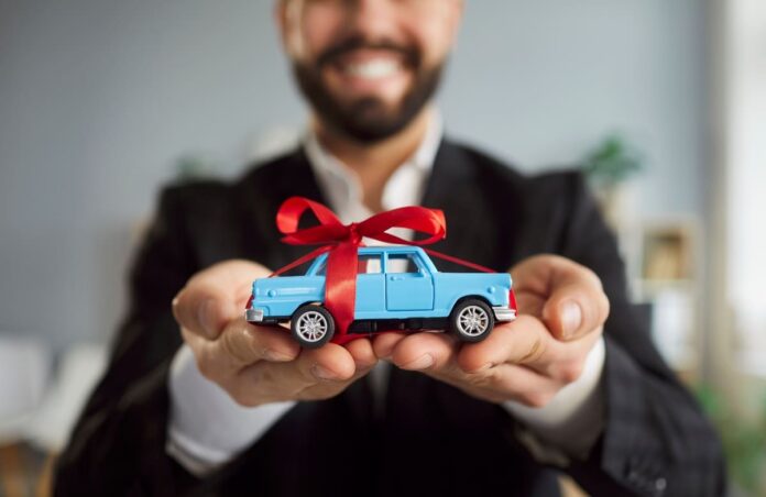 Kaskokindlustuse liisingväärtuskindlustus - punase kinkepaelaga helesinine mudelauto mehe kätel