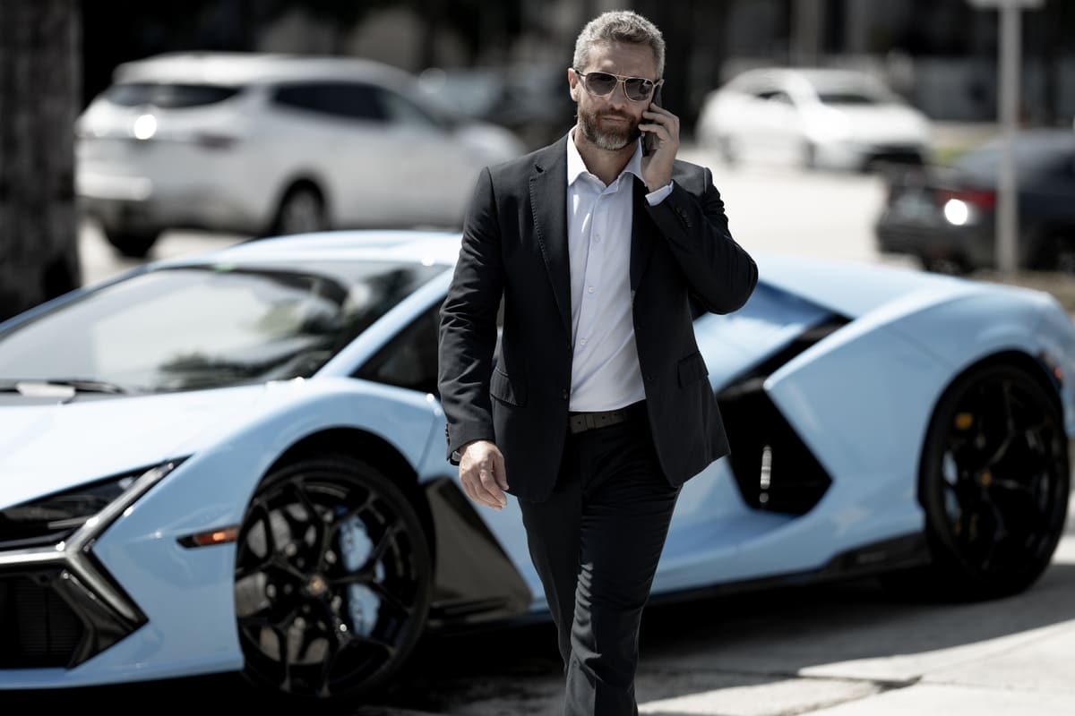 Kaskokindlustuse liisingväärtuskindlustus - ülikonnas mees uhke sportauto juurest lahkumas, telefon kõrva ääres