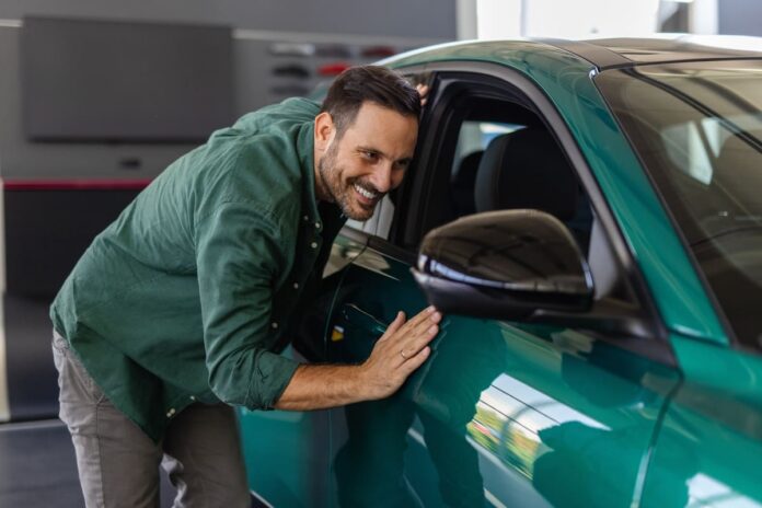 Kaskokindlustuse uusväärtuskindlustus - rohelises kampsunis mees silitab oma rohelist autot