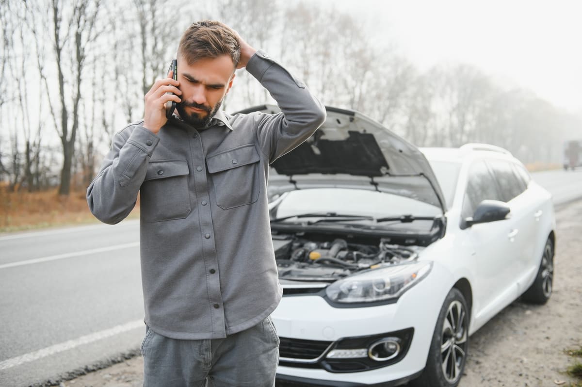 Škoda Octavia kaskokindlustuse tehniline rike - valge auto lahtise kapotiga ja selle ees helistav murelik mees